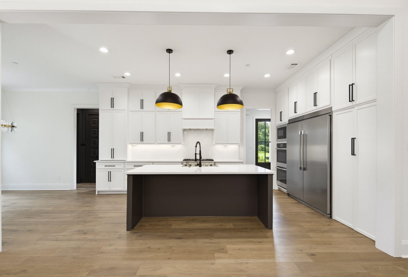 Spacious kitchen featuring a dark-toned island with a light-toned countertop, custom white cabinetry, wood-finish flooring, and stainless steel appliances
