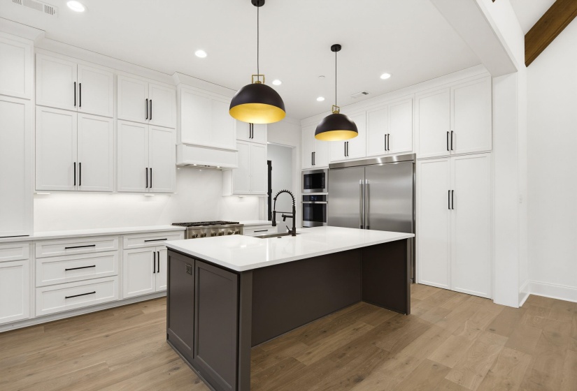 Kitchen featuring a dark gray island with a white countertop and seating, white cabinetry with black hardware, recessed lighting, and stainless steel appliances