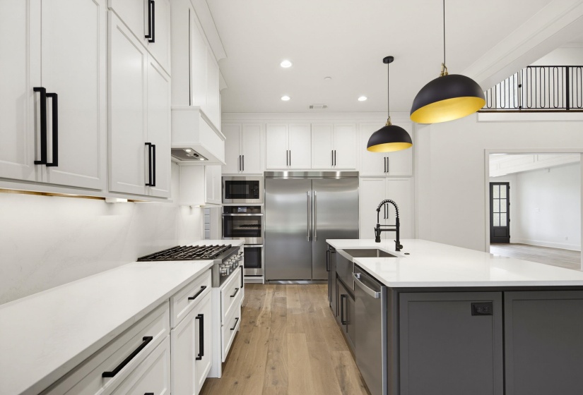 Gourmet kitchen featuring white shaker cabinetry, stainless steel appliances, a gas range with a matching range hood, a spacious island with a single-basin sink, and wood-finish flooring