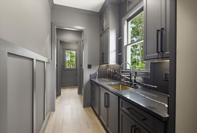 Integrated wet bar featuring a brass sink, a matte black faucet, custom cabinetry, and stone countertops