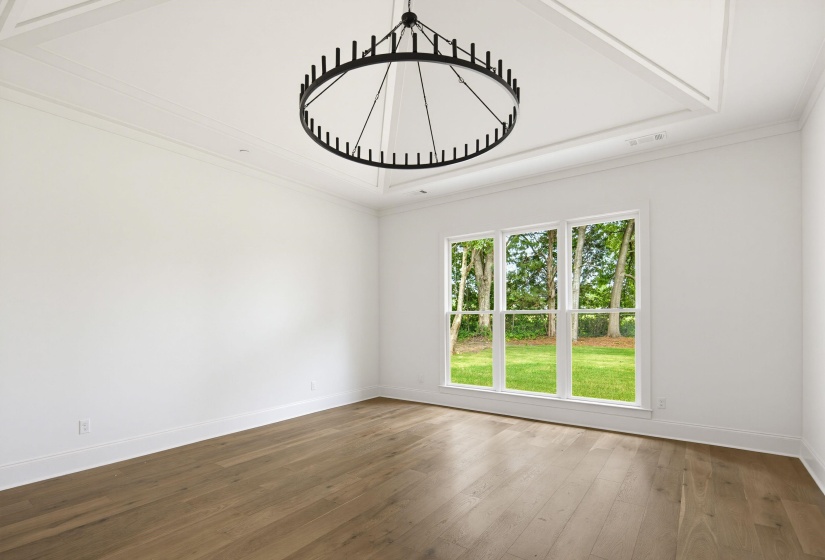 Spacious room featuring wood-finish flooring, white walls, and a prominent black circular chandelier