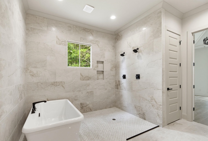 Spacious bathroom featuring large format wall tiles, a freestanding soaking tub with matte black fixtures, an open-concept shower with dual shower heads, and built-in shower niches