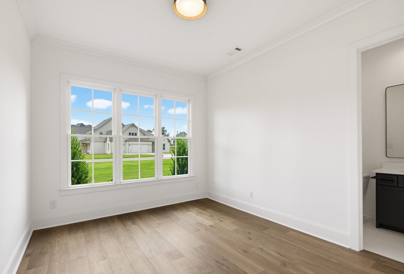 Room featuring wood-finish flooring, white walls, and a multi-pane window overlooking a manicured lawn