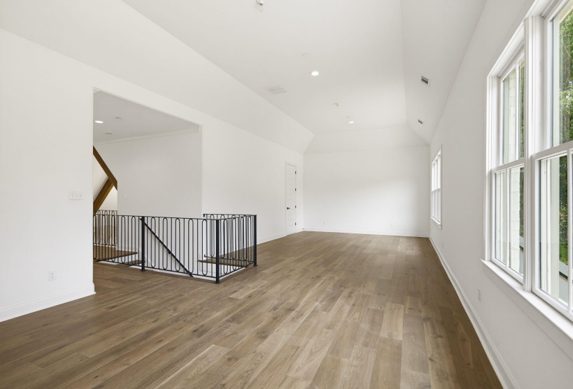 Spacious room featuring wood-finish flooring, white walls, and a vaulted ceiling with recessed lighting