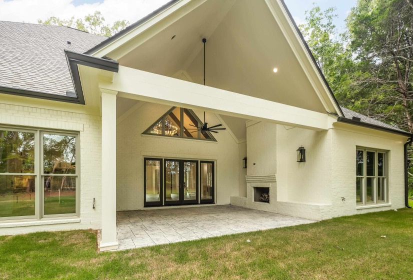 Expansive covered patio featuring a vaulted ceiling with exposed beams, stamped concrete flooring, and a built-in outdoor fireplace