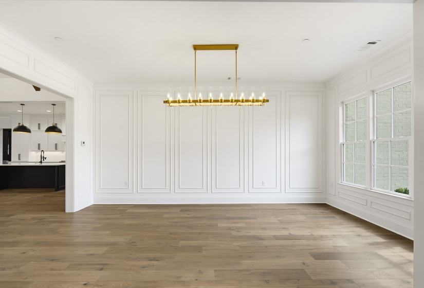 Spacious room featuring wood-finish flooring, white paneled walls, and a contemporary linear chandelier