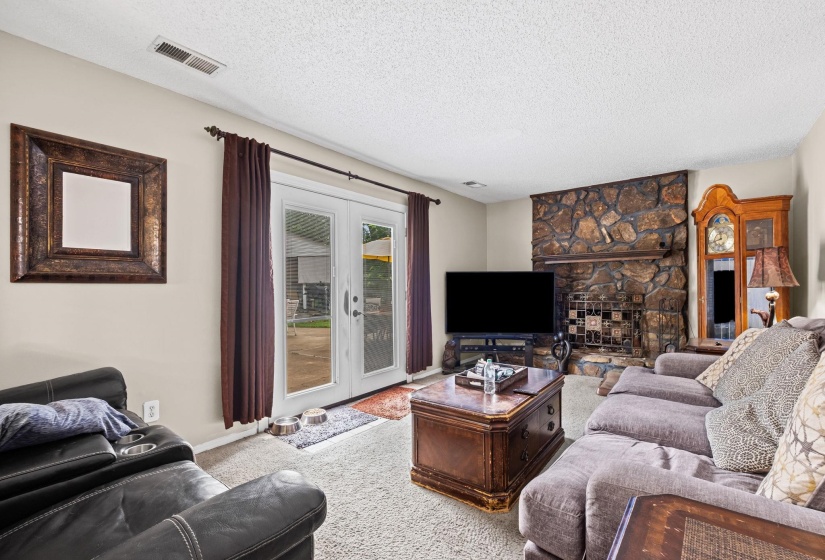 Living area featuring a stone fireplace with a hearth, white walls, and light-colored carpet