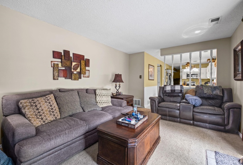 Carpeted living area featuring a decorative half-wall with spindles, warm-toned wall finishes, and a textured ceiling
