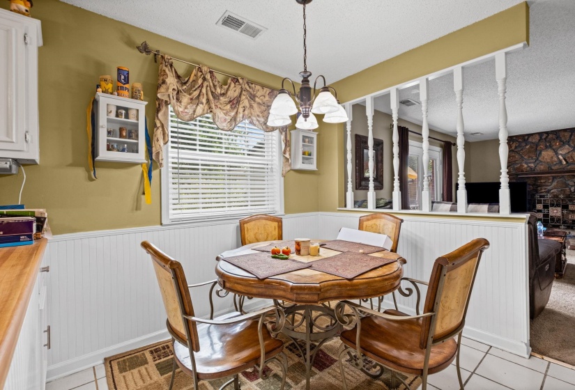 Dining area featuring a window with blinds, a hanging chandelier, wainscoting, and tile flooring