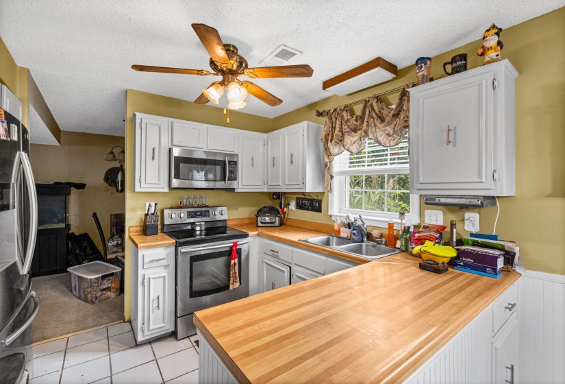 Kitchen featuring white cabinetry, stainless steel appliances, butcher block countertops, and a ceiling fan with integrated lighting