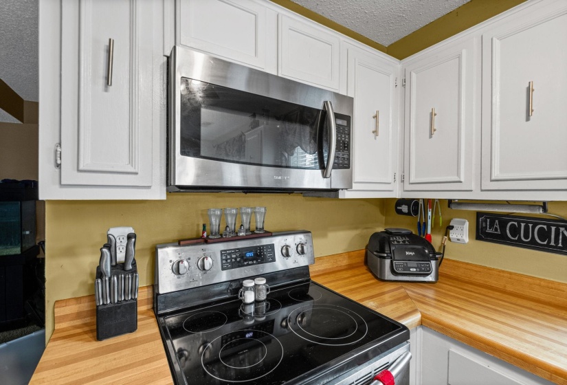 Kitchen featuring white upper cabinetry with brushed nickel hardware, stainless steel over-the-range microwave, wood-finish countertops, and an electric range