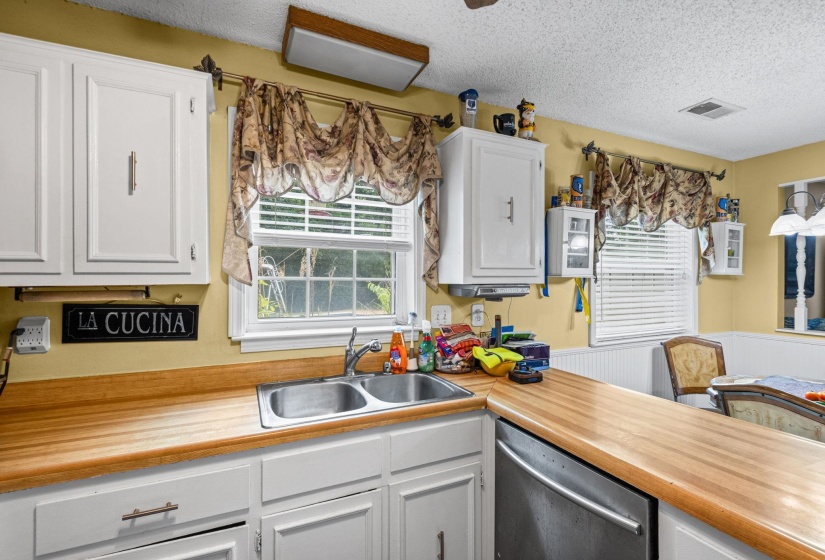Kitchen area featuring a double basin stainless steel sink, wood-finish countertops, white cabinetry, and a built-in dishwasher