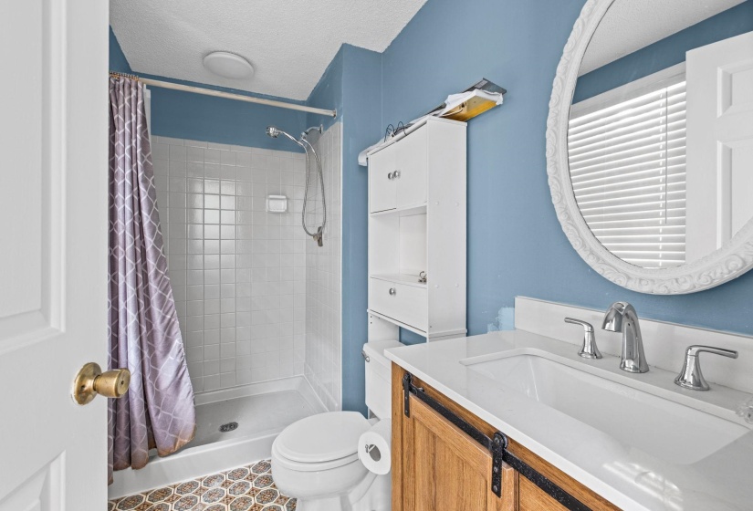 Bathroom featuring a vanity with a white countertop and undermount sink, an ornate white framed mirror, and a white tile shower with a handheld showerhead