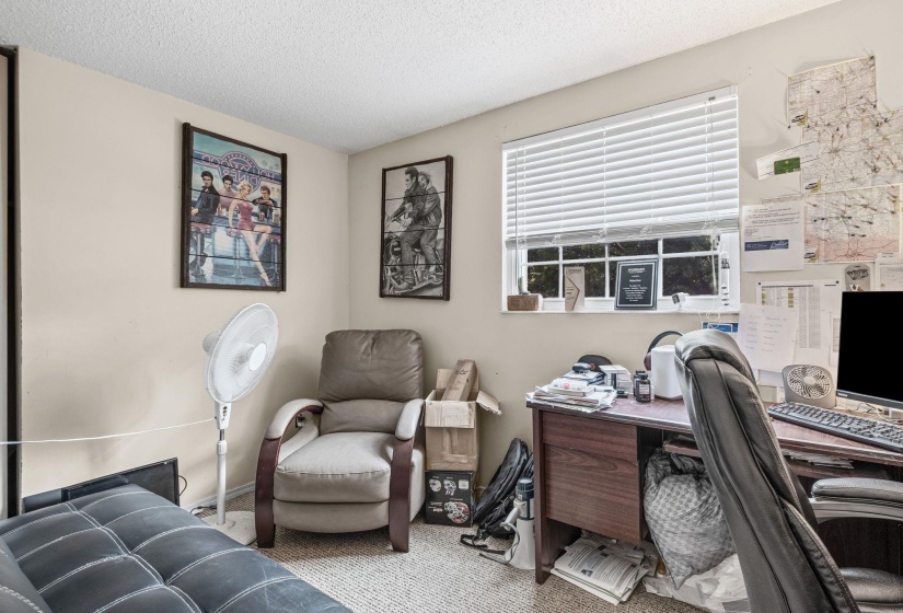 Light-colored walls with a textured ceiling, featuring a window with horizontal blinds