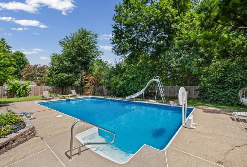 Rectangular inground pool featuring concrete surround, privacy fencing, and mature perimeter trees