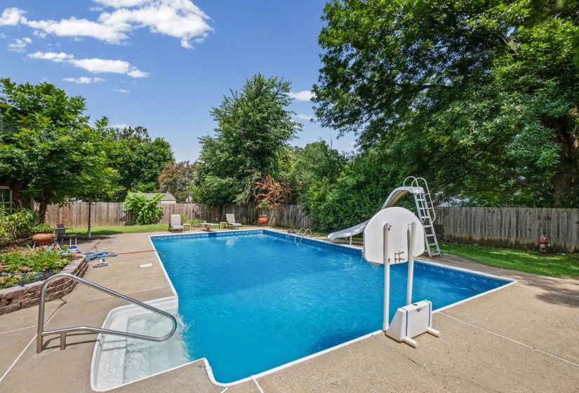 In-ground swimming pool featuring a concrete deck, built-in steps, and a perimeter fence