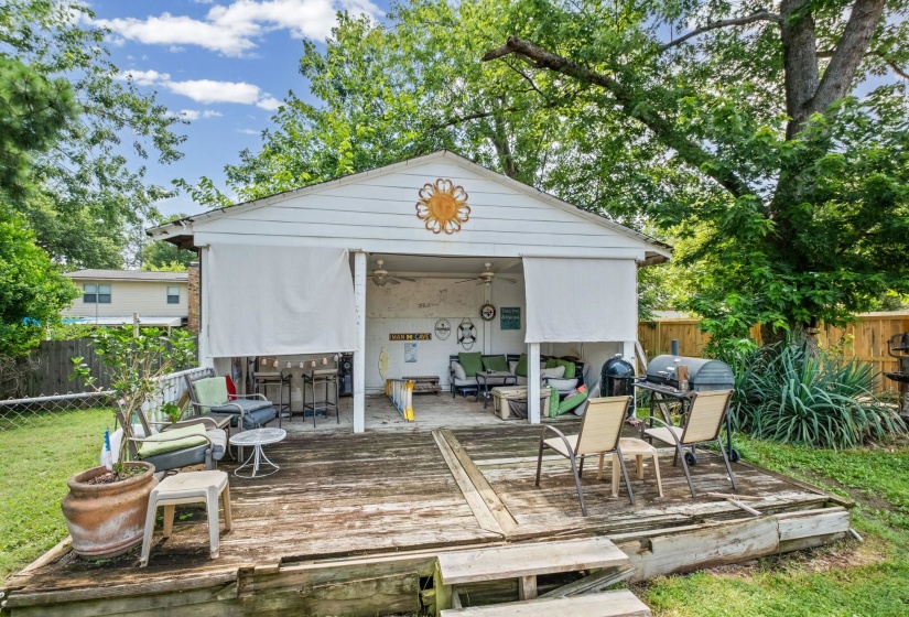 Detached outbuilding with a covered patio area, featuring a wood-finish deck and surrounding mature trees