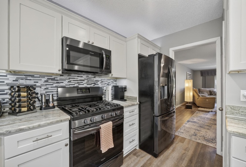 Kitchen featuring white cabinetry, granite countertops, a tiled backsplash, and stainless steel appliances including an oven with gas cooktop, microwave, and refrigerator