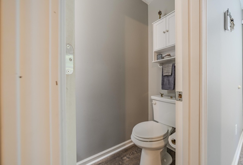 Powder room with wood-finish flooring, neutral gray walls, white trim, and a white toilet