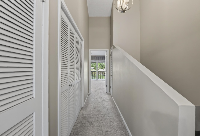Carpeted hallway with louvered bi-fold closet doors, staircase wall, and overhead light fixture leading to Primary Bedroom, Bath and covered Balcony