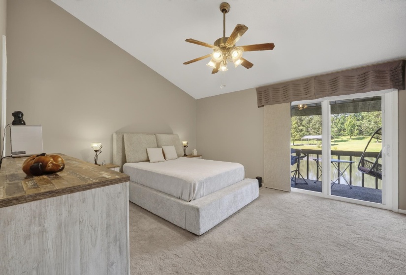 Vaulted ceiling with a ceiling fan, carpeted flooring, and a sliding glass door leading to an outdoor covered balcony with waterview.