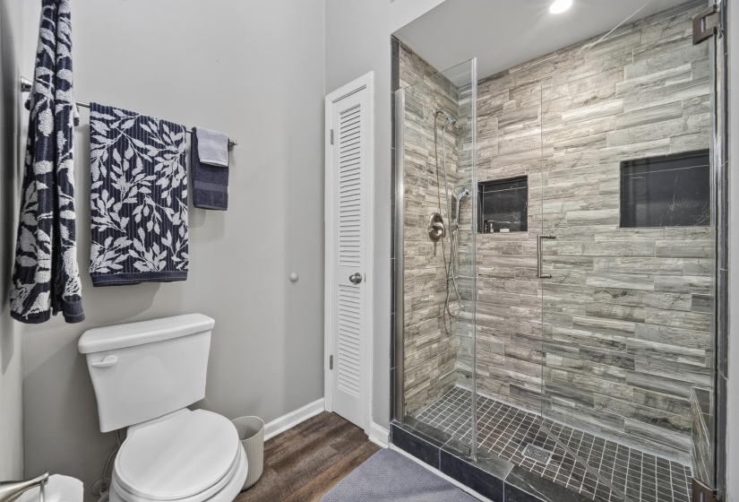 Glass-enclosed shower featuring stacked stone-look wall tile, dual recessed niches, and a tiled shower pan