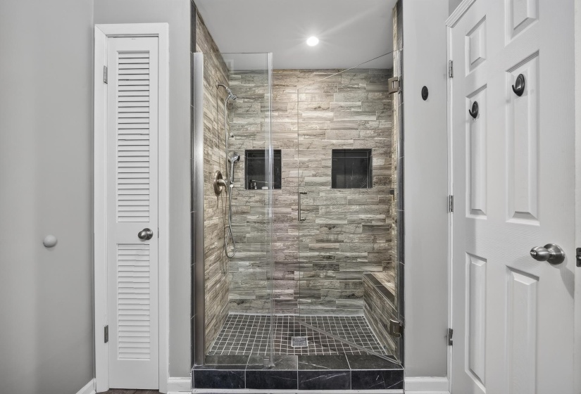 Glass-enclosed shower featuring stacked stone-look wall tile and a built-in bench
