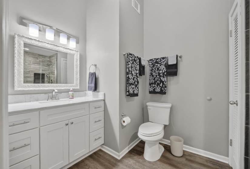 Bathroom featuring a spacious white vanity with a single sink, an ornate framed mirror, and a four-light fixture, granite countertop