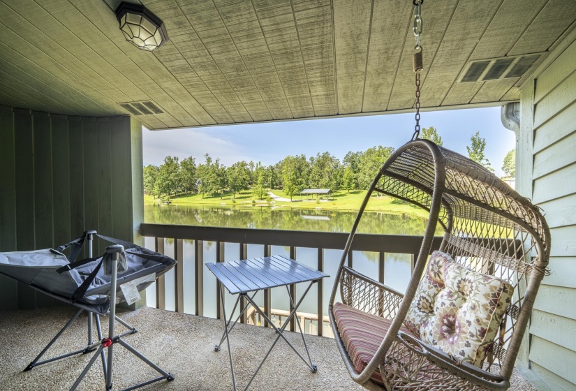 Covered outdoor balcony with a tranquil water feature backdrop, featuring a slatted ceiling, exterior wall light, and wood-finish railing.  Off Primary Bedroom