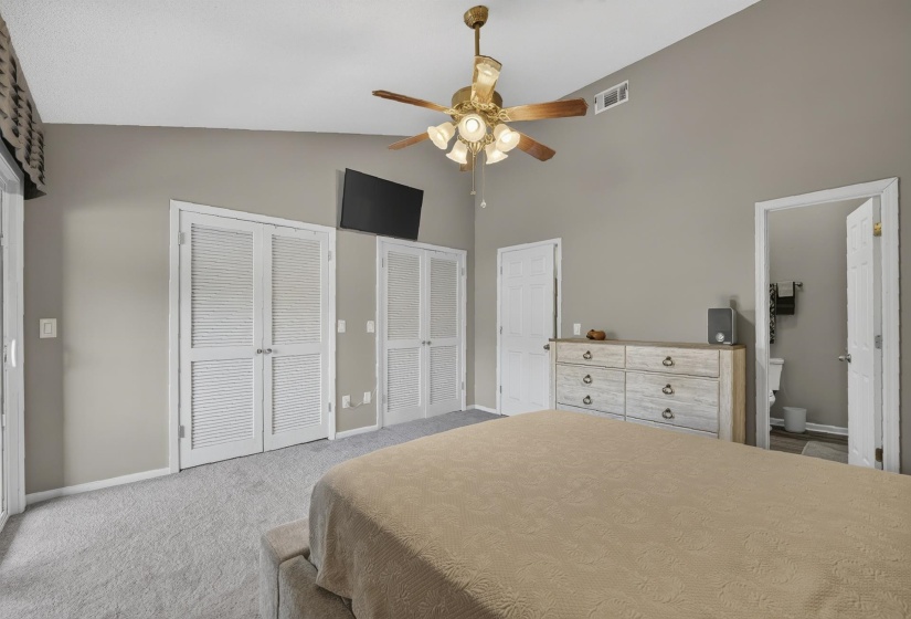 Spacious bedroom featuring light grey carpeting, painted walls, a vaulted ceiling, and dual louvered closet doors