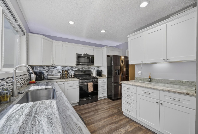 Kitchen featuring white shaker cabinetry, stainless steel appliances, wood-finish flooring, undermount sink, and granite countertops