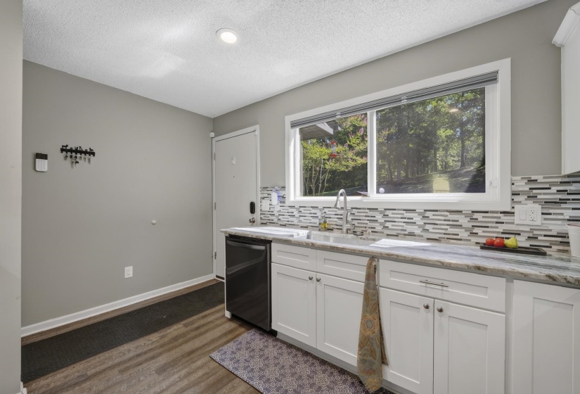 Kitchen featuring white cabinetry, a single basin sink with a chrome faucet, a black dishwasher, and wood-finish flooring