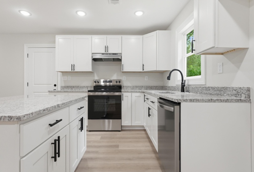 Contemporary kitchen featuring white cabinetry with black hardware, stainless steel appliances, speckled stone countertops, wood-finish flooring, and recessed lighting