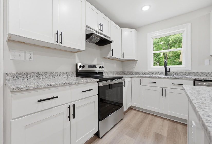 Contemporary kitchen featuring white shaker cabinetry with matte black hardware, granite countertops, and wood-finish flooring