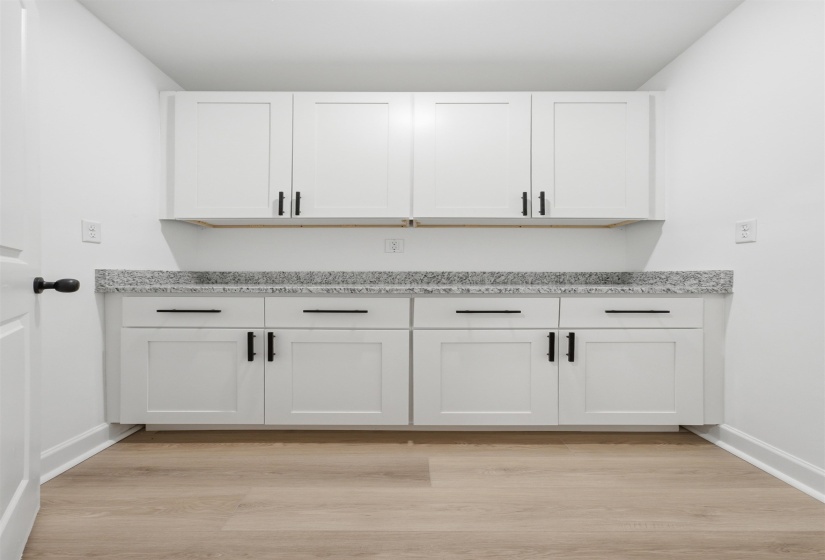 Cabinetry featuring white shaker-style doors with matte black hardware, a light-toned countertop, and wood-finish flooring