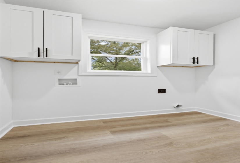 Laundry room featuring wood-finish flooring, white walls, and white upper cabinetry with black hardware