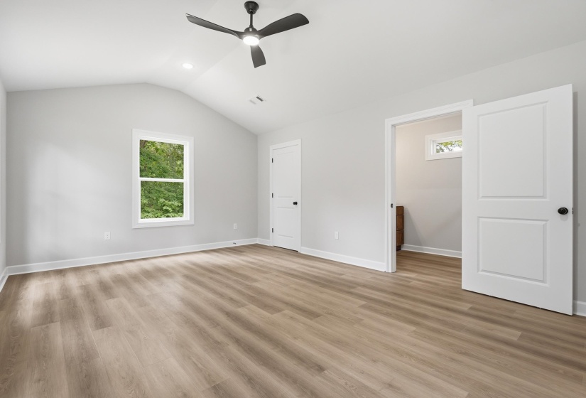 Spacious room featuring vaulted ceilings, wood-finish flooring, and a modern ceiling fan