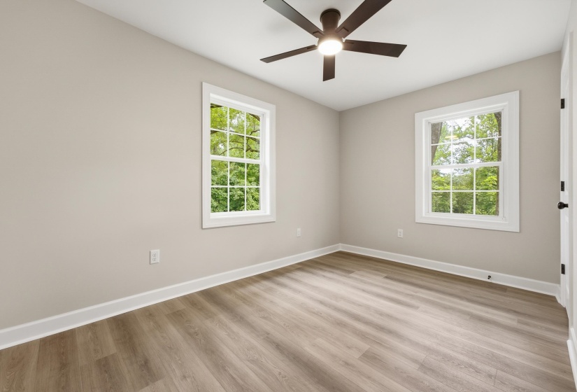 Spacious room featuring wood-finish flooring, two large windows, a ceiling fan with integrated lighting, neutral wall tones, and white trim