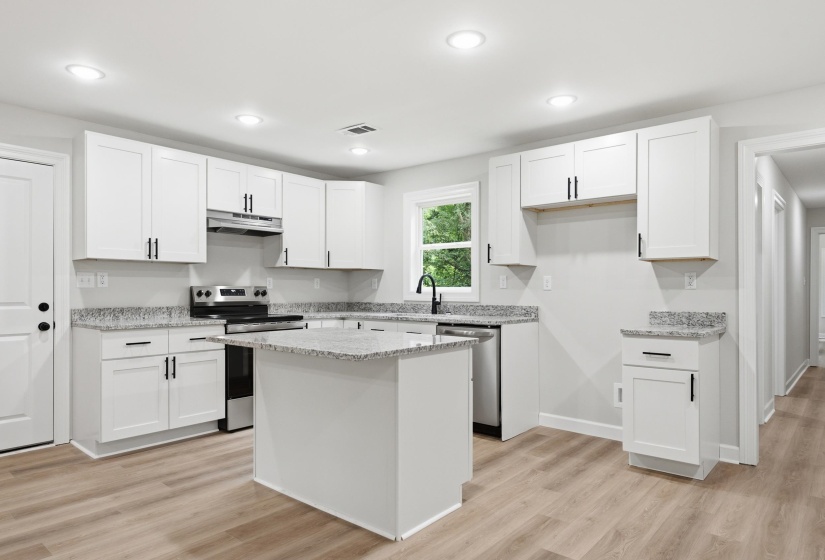 Kitchen featuring an island, white shaker cabinetry, speckled countertops, stainless steel appliances, and wood-finish flooring