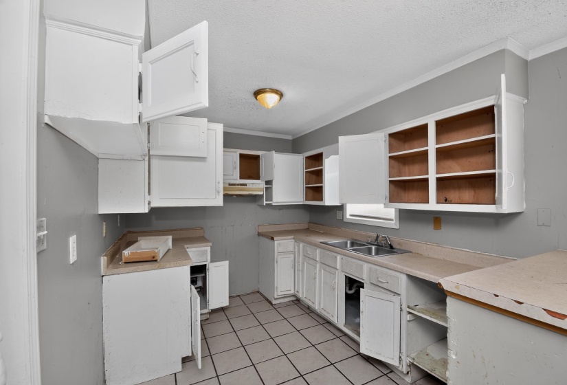 Kitchen featuring white cabinetry with open doors, light-toned countertops, a double basin sink with chrome faucet, and tiled flooring