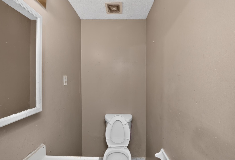 Compact bathroom featuring a white toilet, framed mirror, and beige wall paint
