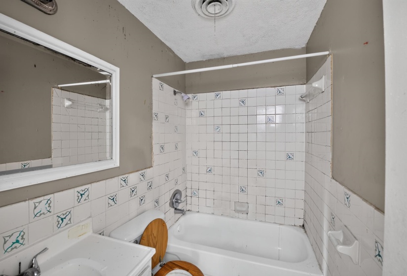 Bathroom featuring a white porcelain tub, white tiled surround with blue accent tiles, and a white vanity with an integrated sink