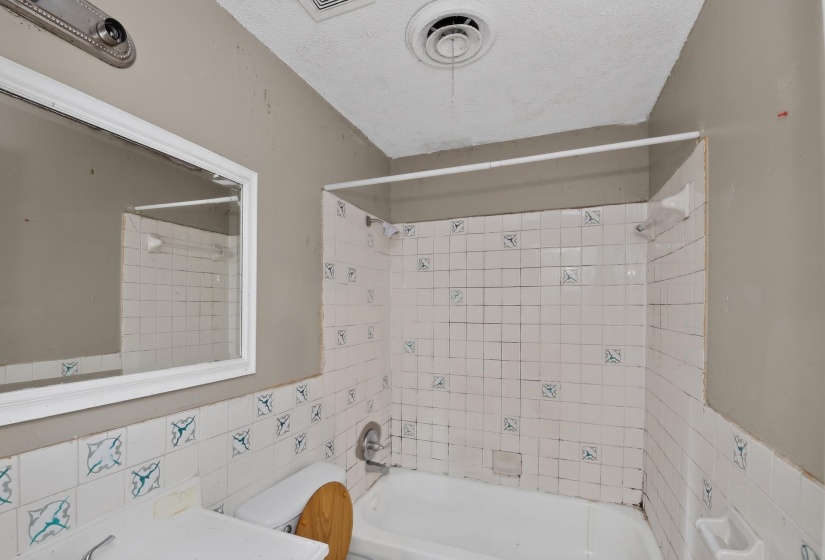 Bathroom featuring white ceramic tiled shower surround with accent tiles, a white bathtub, and a wall-mounted mirror