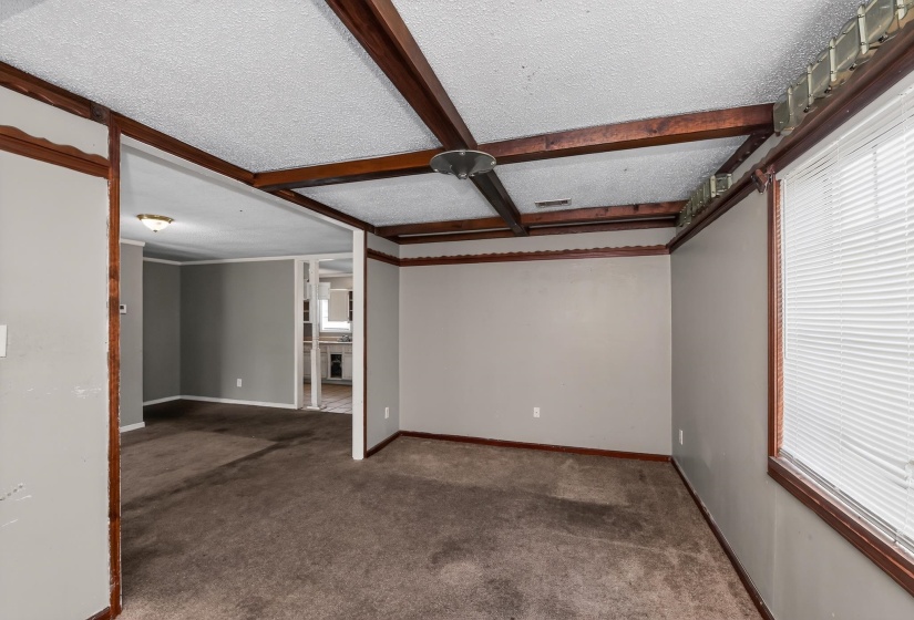 Spacious interior room featuring textured ceilings with exposed faux wood beams, a large window with blinds, and neutral-toned wall paint