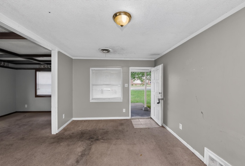Entry room featuring a ceiling-mounted light fixture, neutral-toned walls, and a visible doorway to an additional room