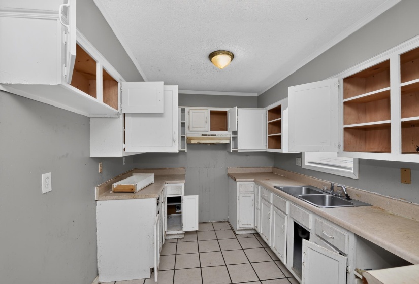 Kitchen featuring extensive white cabinetry, a double basin stainless steel sink, beige countertops, and square tile flooring