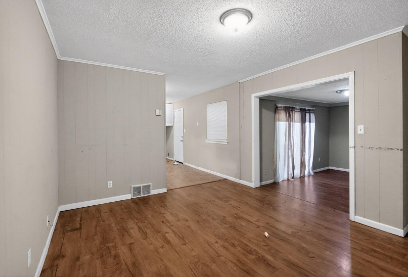 Spacious room featuring wood-finish flooring, light neutral wall paneling, white trim, and a flush-mount ceiling light fixture