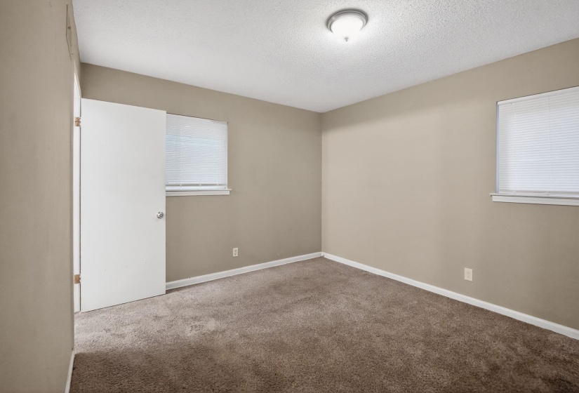 Neutral-toned interior room featuring two windows with horizontal blinds, a brown carpeted floor, and a white ceiling with a flush-mount light fixture