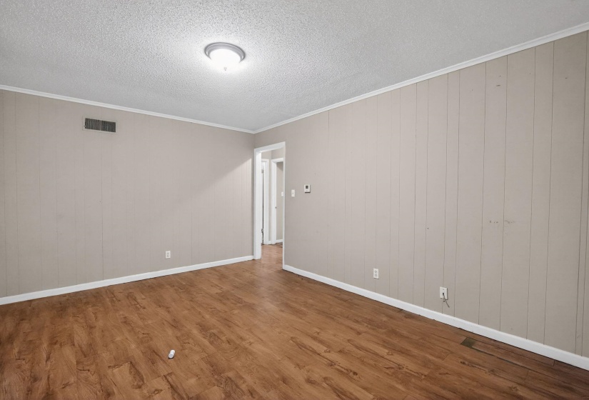 Spacious room featuring wood-finish flooring, light-toned walls, white baseboards, and crown molding