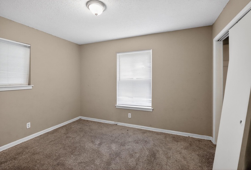 Carpeted room featuring two windows with horizontal blinds, neutral wall paint, and white trim